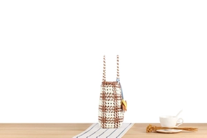 Detail of woven tote bag with checkered pattern and yellow flower charm on wooden table