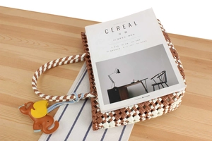 Close-up of brown and white woven leather tote bag with elephant charm on wooden table