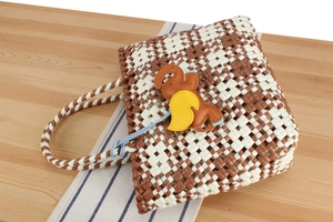 Detail of woven plastic tote bag with brown and white diamond pattern and elephant charm