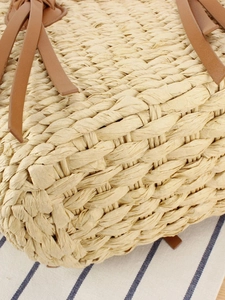 Handwoven straw tote bag with brown leather handles on blue striped fabric background