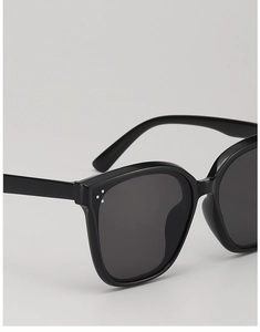 Detail shot of black oversized sunglasses showing silver rivet accents and dark lenses