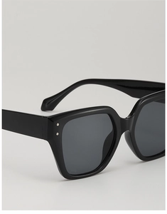 Close-up of black glossy oversized square sunglasses with metallic rivet details