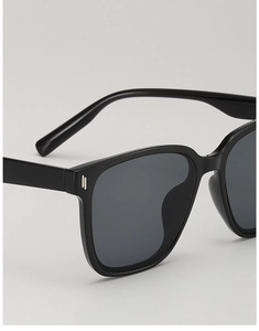 Détail de lunettes de soleil noires surdimensionnées avec rivets métalliques verticaux argentés