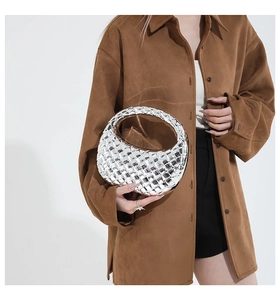 Detail view of a silver woven crescent handbag with metallic finish held by a model