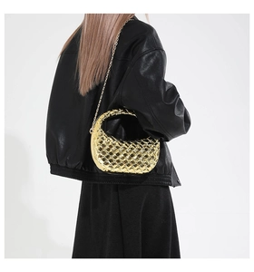Dettaglio pochette intrecciata dorata con tracolla a catena e giacca nera di moda