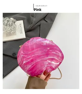 Pink marble texture acrylic shell evening bag with golden chain on grey suit background
