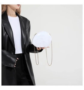 Detail of white marble shell evening bag with gold chain strap on black leather jacket