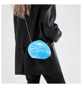 Detail of blue marble acrylic clutch bag with gold chain strap on a black leather jacket