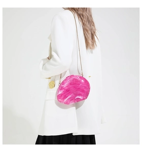 Detailed shot of pink marble acrylic evening bag with gold chain strap on white blazer