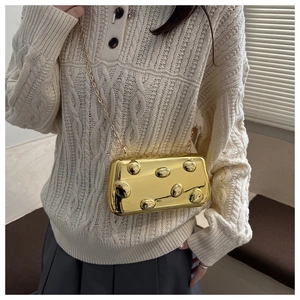 Detail einer goldenen Metallic-Box-Clutch mit Noppenstruktur und feinem Kettenriemen