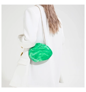 Detail of green marble acrylic clutch bag with gold chain strap on white blazer
