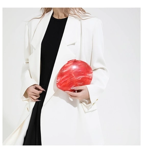 Model holding a red marble acrylic egg-shaped evening clutch with organic textures