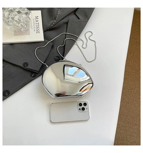 Silver metallic egg-shaped clutch bag with snake chain shown next to a smartphone