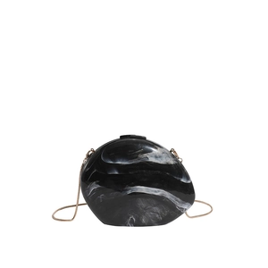 Macro detail of acrylic dinner clutch showing black and white marble texture and gold chain
