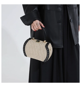 Detail of cylindrical straw handbag with black leather trim and gold rivet accents