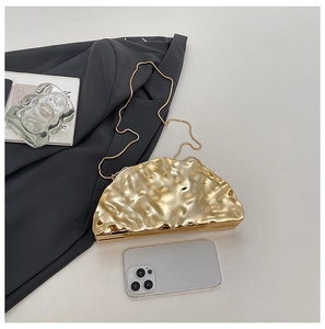 Golden semicircular evening clutch with hammered metal texture next to a phone for scale
