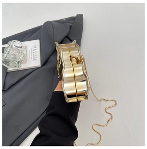 Detail of gold wave-edge evening bag featuring a polished metal finish and snake chain strap