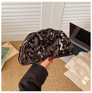 Detail of glossy black shell evening bag with ripple texture and gold chain strap