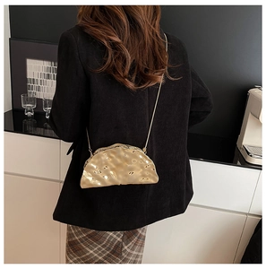 Detail of golden cloud clutch with irregular texture shown on a crossbody chain strap