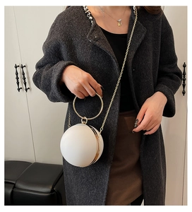 Detail view of a white spherical evening bag featuring a gold ring handle and chain strap