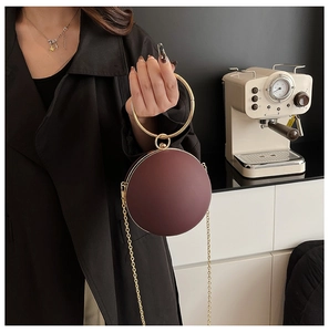 Detail of round burgundy clutch with golden ring handle and elegant metal chain strap