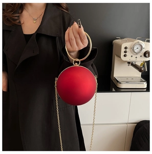 Detail of red spherical evening clutch bag with gold ring handle and chain strap
