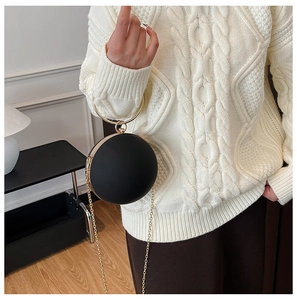Detail of round sphere clutch bag in matte black with elegant gold circular handle