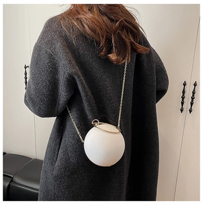 Detailed view of a white spherical clutch with gold chain strap on a dark grey wool coat