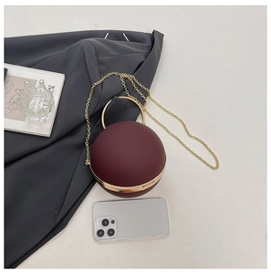 Detail view of burgundy spherical evening bag with golden ring handle and metal chain