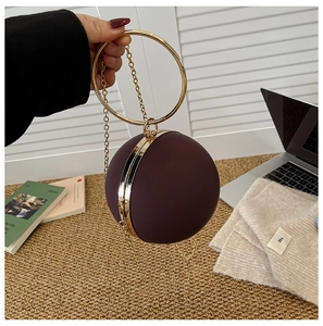 Detail of burgundy spherical evening bag with oversized gold metal circular handle