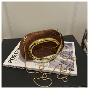 Détail d'une pochette en velours marron avec anneau doré et chaîne serpent sur un magazine