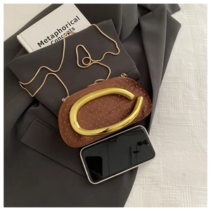 Détail de pochette en velours marron avec poignée dorée en U et strass sur un blazer