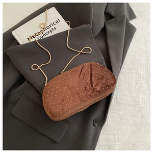 Détail d'une pochette de soirée en velours marron avec clous dorés et chaîne sur blazer