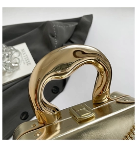 Détail d'un sac de soirée doré avec poignée ondulée et garniture en strass brillants