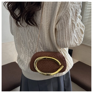Détail d'un sac bandoulière en daim marron avec ornement doré porté sur un pull blanc chiné