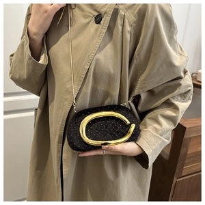 Détail de pochette strass noire avec poignée en C dorée portée sur un manteau beige