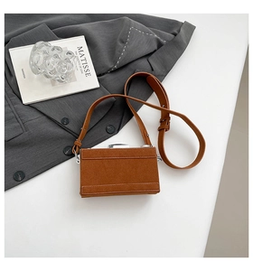 Détail d'un sac bandoulière créatif en daim marron posé sur une veste de costume grise