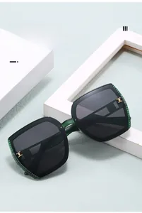 Close-up of dark green square sunglasses with golden metal hinge detail on stone pedestal