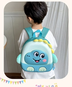 Child wearing a green dinosaur eggshell backpack featuring 3D scales and padded straps