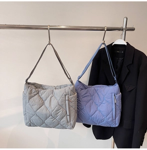 Detail of gray and purple quilted nylon tote bags with side zipper pockets on rack