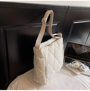 Close-up of beige quilted puffer bag with rhombus texture and adjustable strap on a bed
