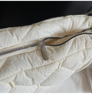 Macro view of white quilted nylon bag with silver square metal zipper detail
