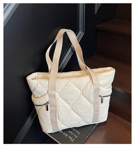 Detail of cream quilted tote bag featuring large diamond stitching and metal zippers