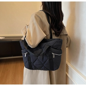 Close-up of black quilted puffer tote bag featuring side metal zipper pockets and wide straps