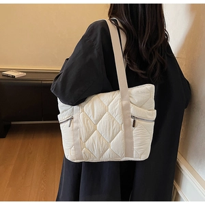 Quilted ivory puffer tote bag with silver zippers shown on shoulder over black coat