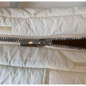 Detail of silver metal zipper and quilted diamond fabric on a cream puffer tote bag