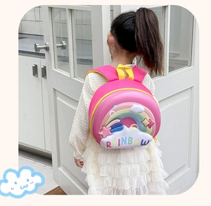 Pink EVA hardshell rainbow backpack for toddlers worn by child in bright room