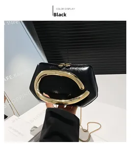 Detail view of a black glossy handbag featuring an oversized gold metal handle and chain