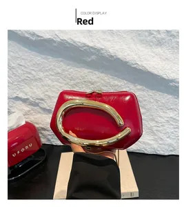 Detail of red leather clutch featuring a large irregular gold metal handle and polished finish