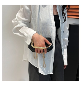 Detail of minimalist black leather handbag with striking gold U-shaped metal handle